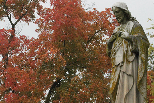 A weathered stone sculpture of the Sacred Heart of Jesus sets apart the autumn colors in St. Peter Cemetery in Jefferson City.